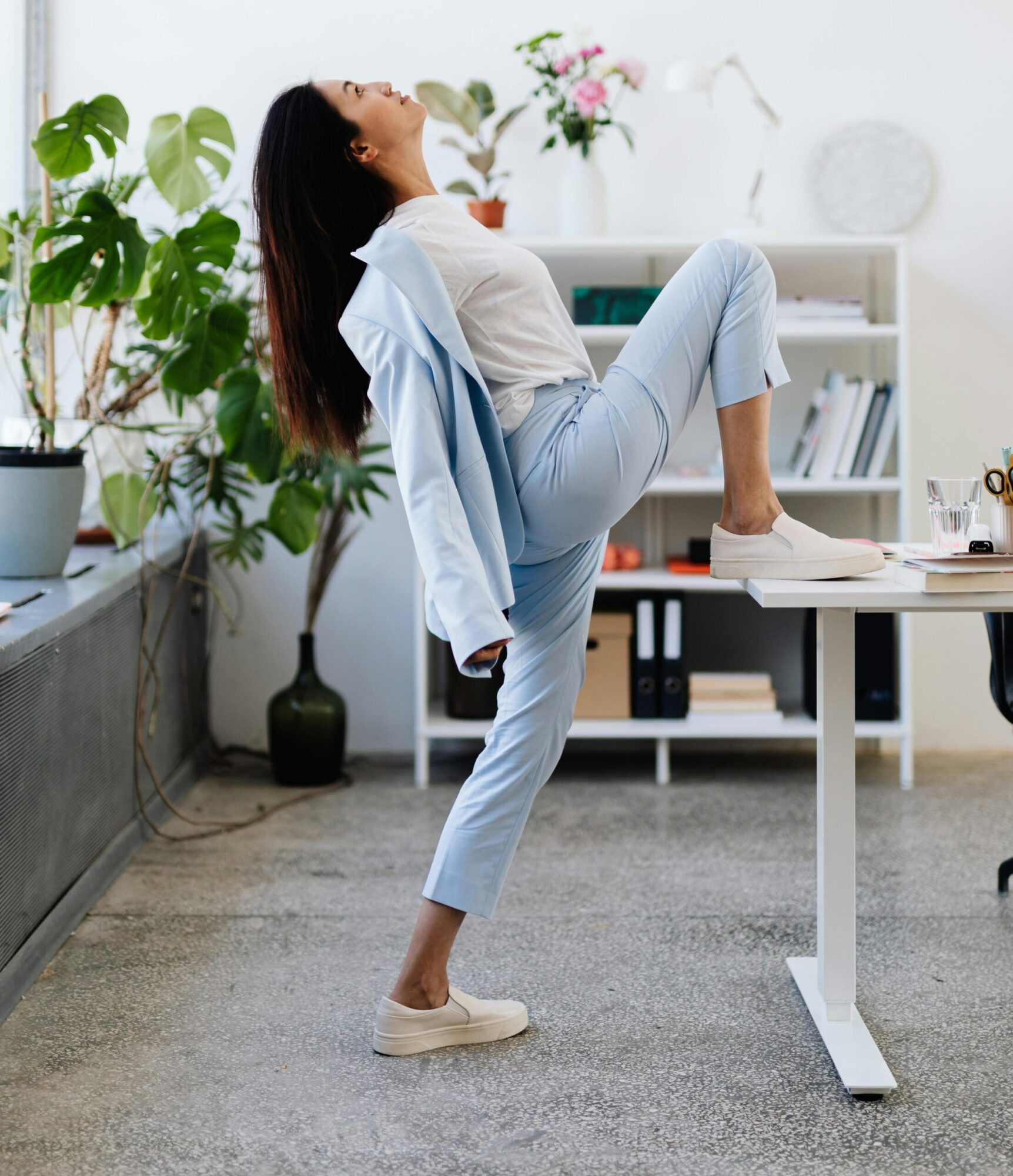 une femme en tailleur bleu ciel s'étire, un pied posé sur le bureau